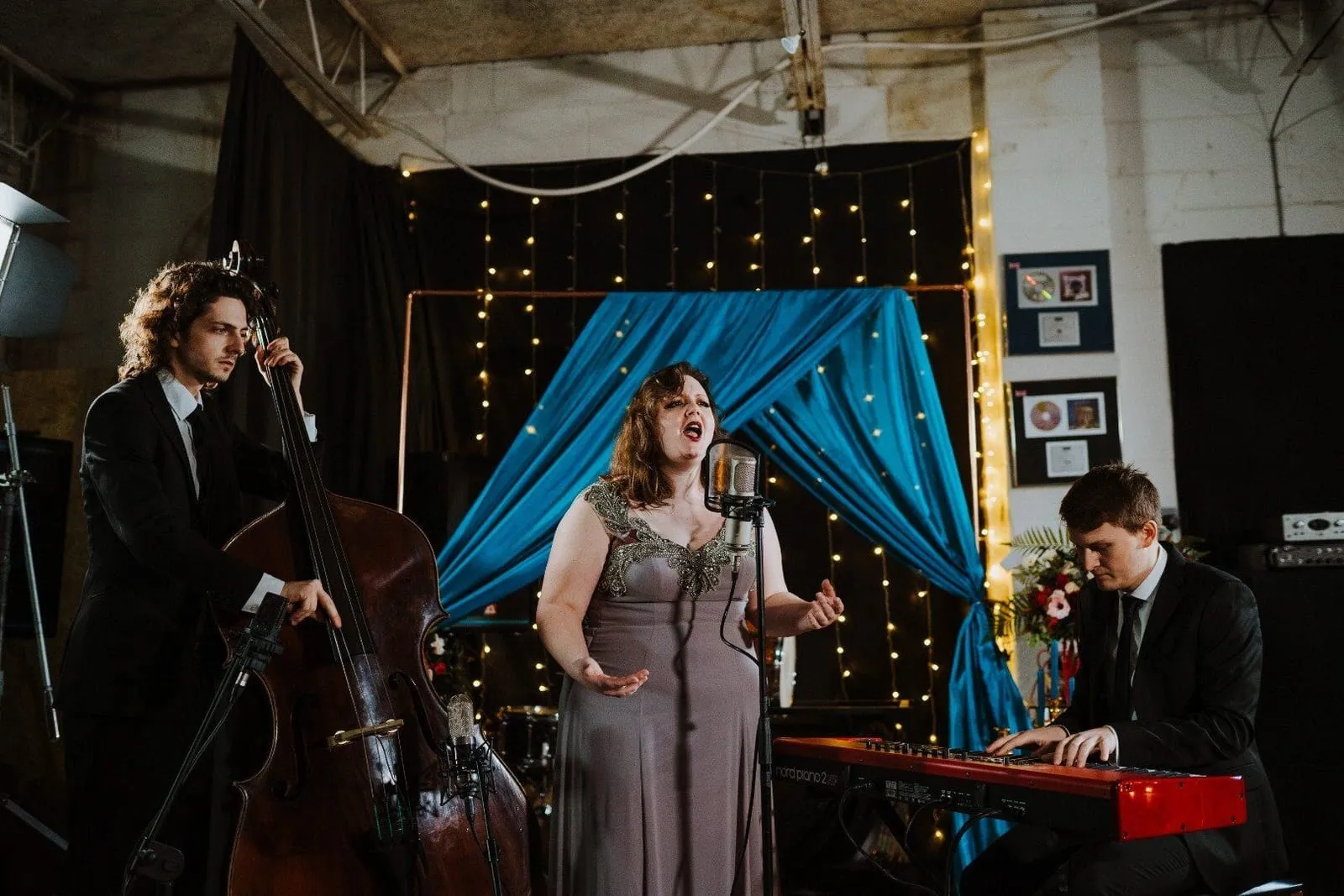 band with a singer, cellist and keyboard player performing in a fairy light lit room 