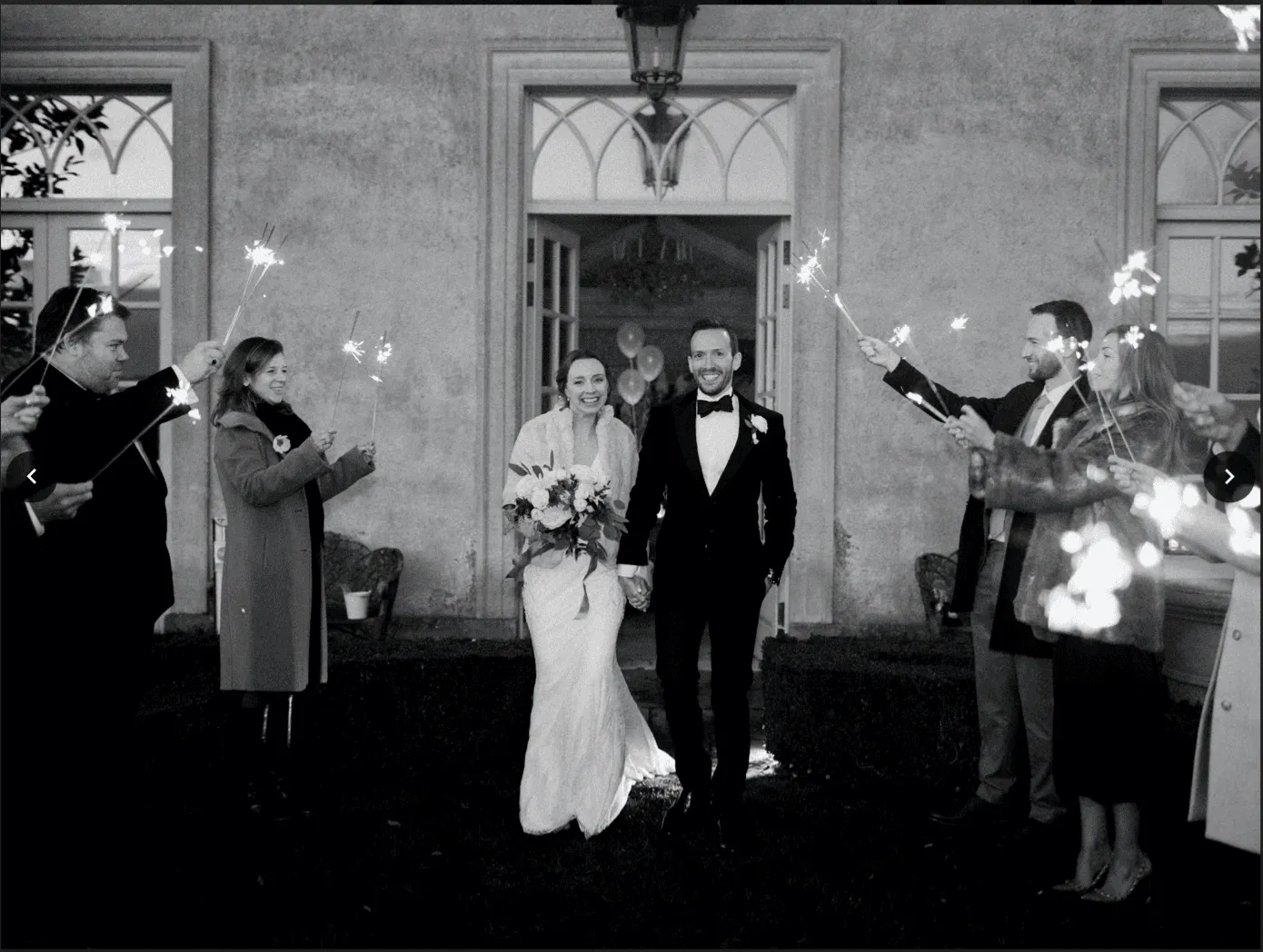 black and white photo of bride and groom walking between their guests holding sparklers