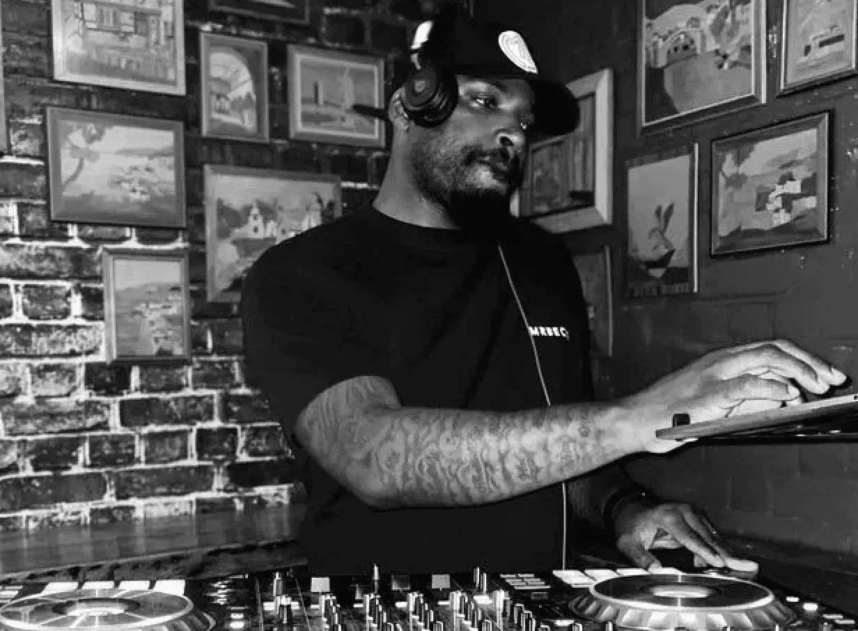 close up of DJ on the decks with a brick wall background with photos hanging