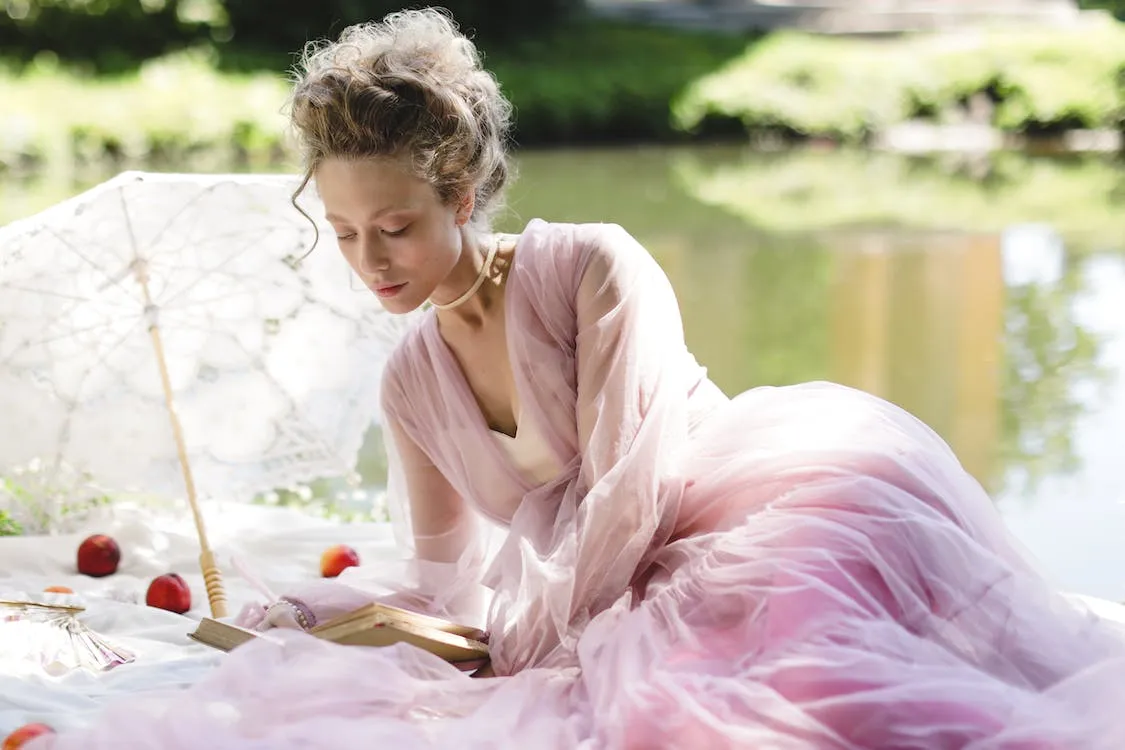 blonde woman reading a book in a garden on sunny day in regency era dress