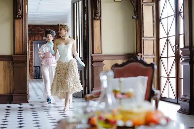 two women in regency era attire dancing through the hallways of an old house