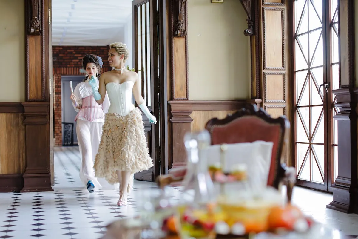 two women in regency era attire dancing through the hallways of an old house
