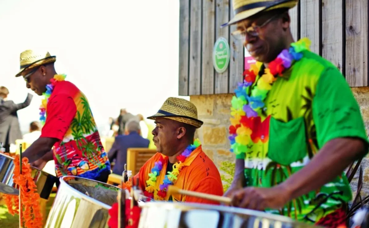 ALT="close up of three men in Hawaiians shirts playing steel drums"