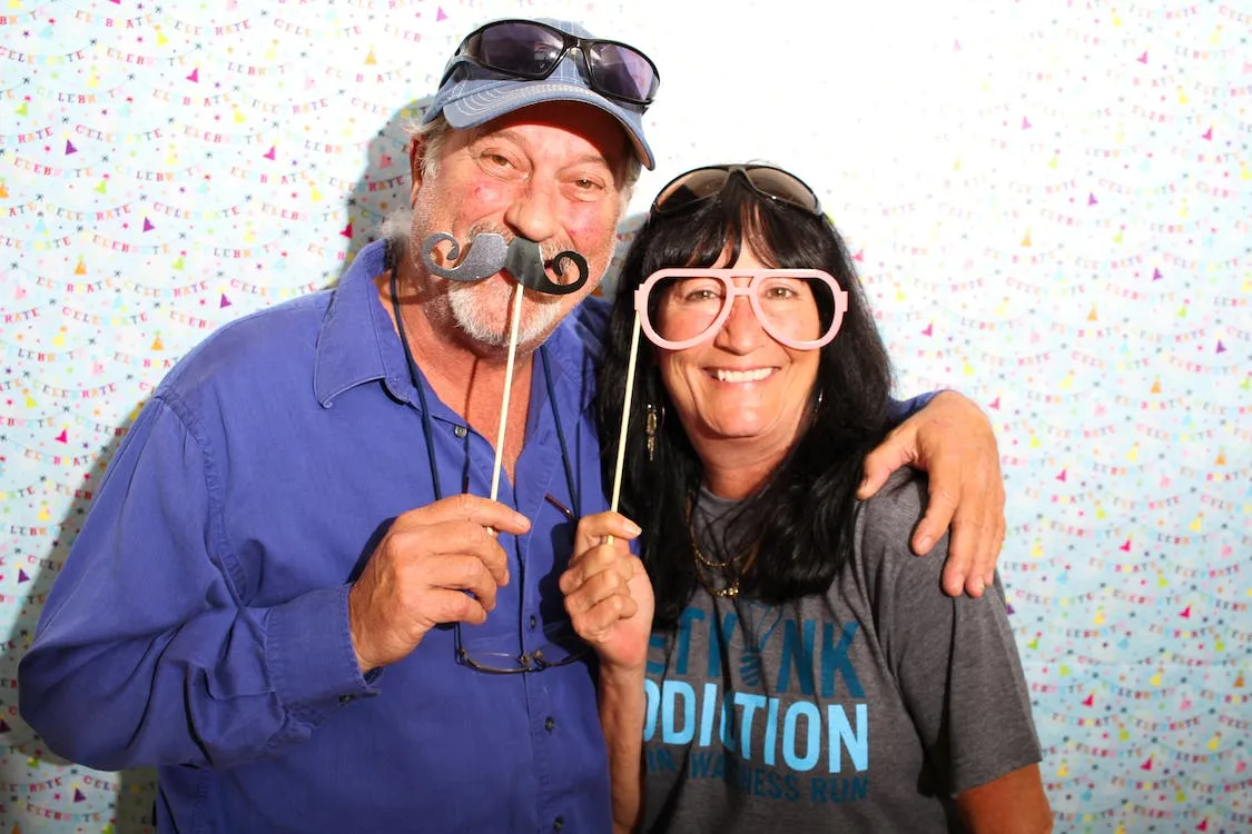 older couple using a photobooth with moustache and glasses props