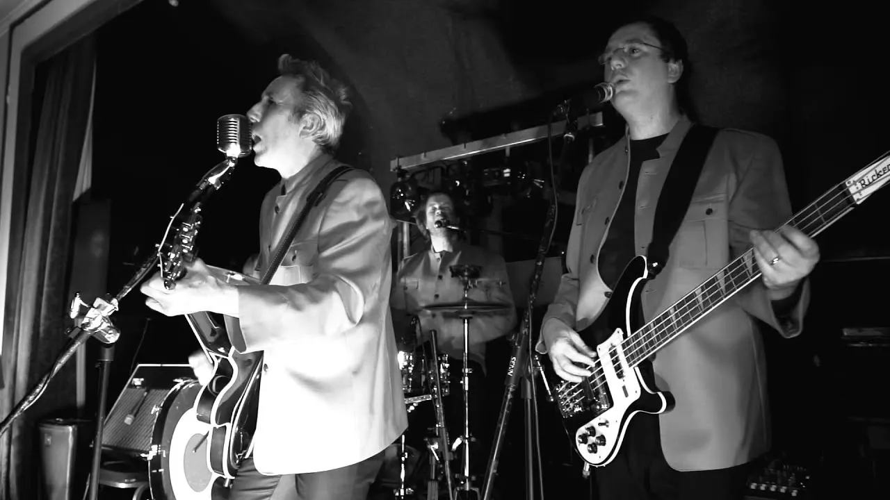 all male band with lead singer singing into a mic and a guitar in black and white